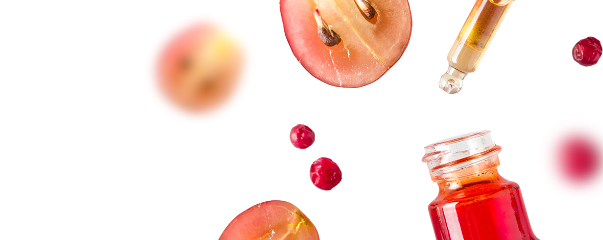 Extrakt z hroznových šupiek kvapká z kvapátka do nádoby, na bielom pozadí vo vzduchu lietajú plody hrozna.